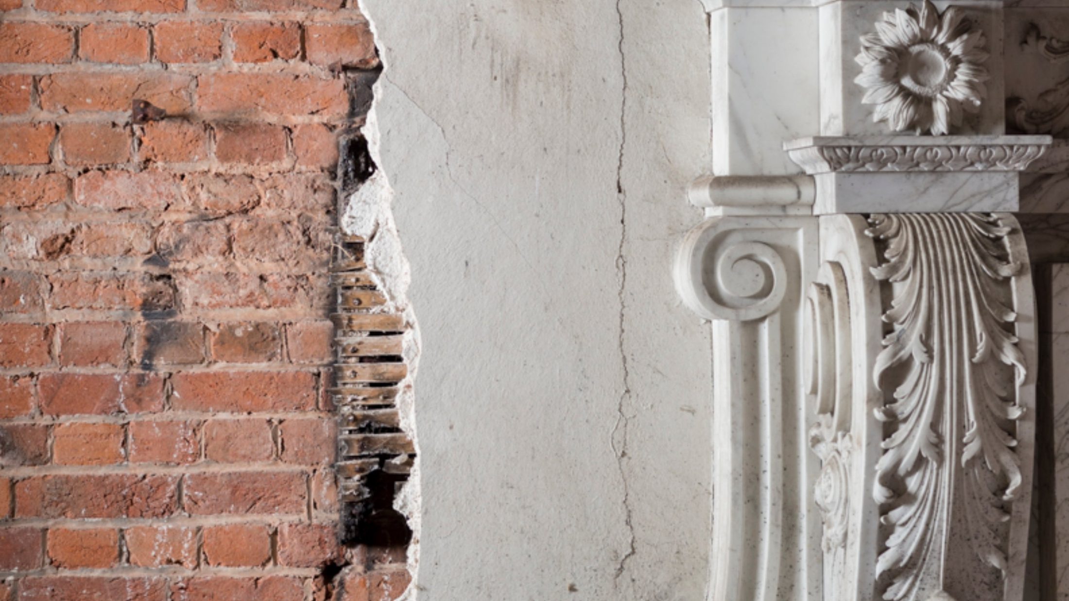 Exposed brick wall alongside an ornate carved marble fireplace surround, showing old and new construction side by side