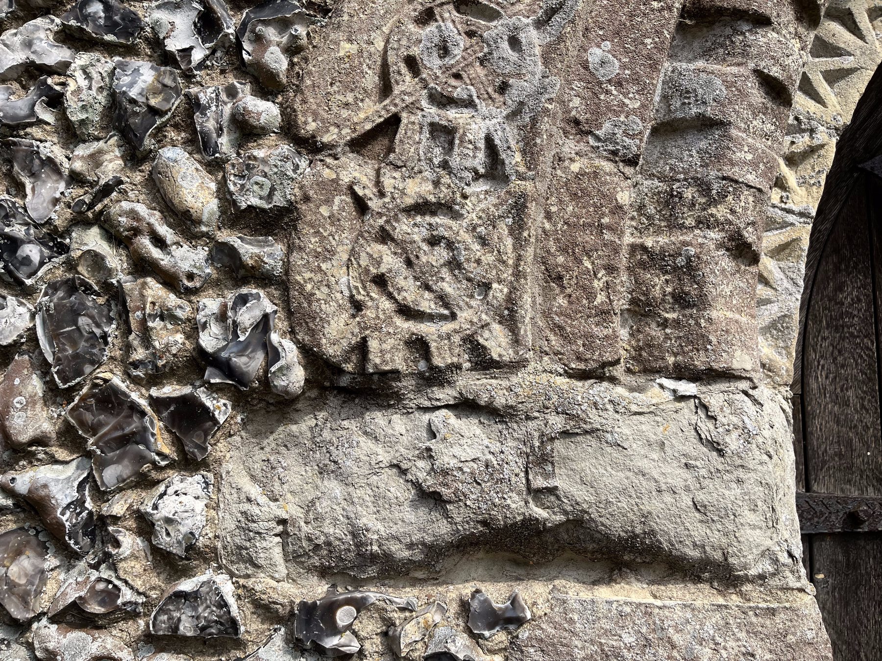 Close detail of a carved medieval consecration cross on ashlar masonry, set beside a traditional knapped-flint wall, showing the fine historic stonework this service protects