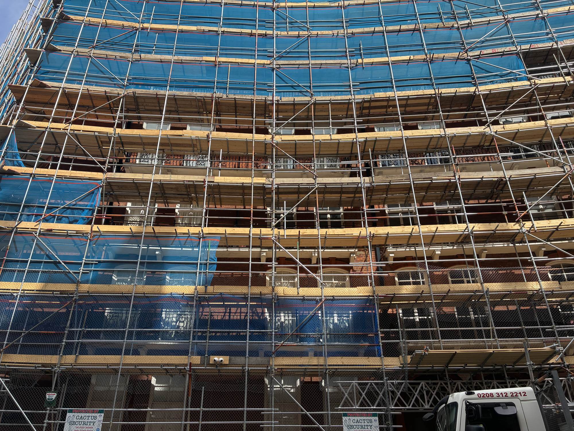 Historic red-brick building facade wrapped in construction scaffolding during a refurbishment project