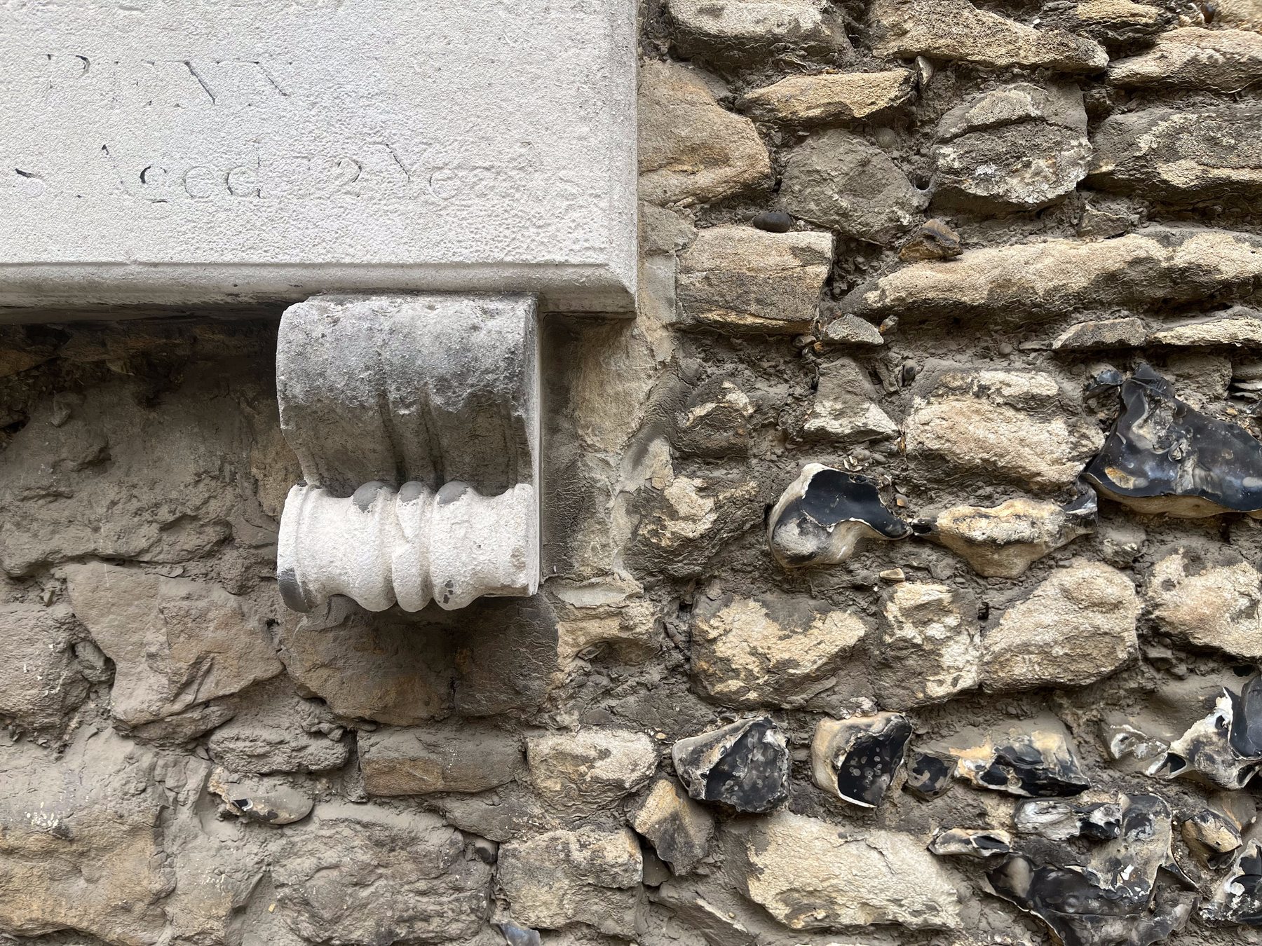 Close inspection of a carved stone corbel and inscribed plaque set into a historic knapped-flint wall, showing the kind of detailed material survey this service involves